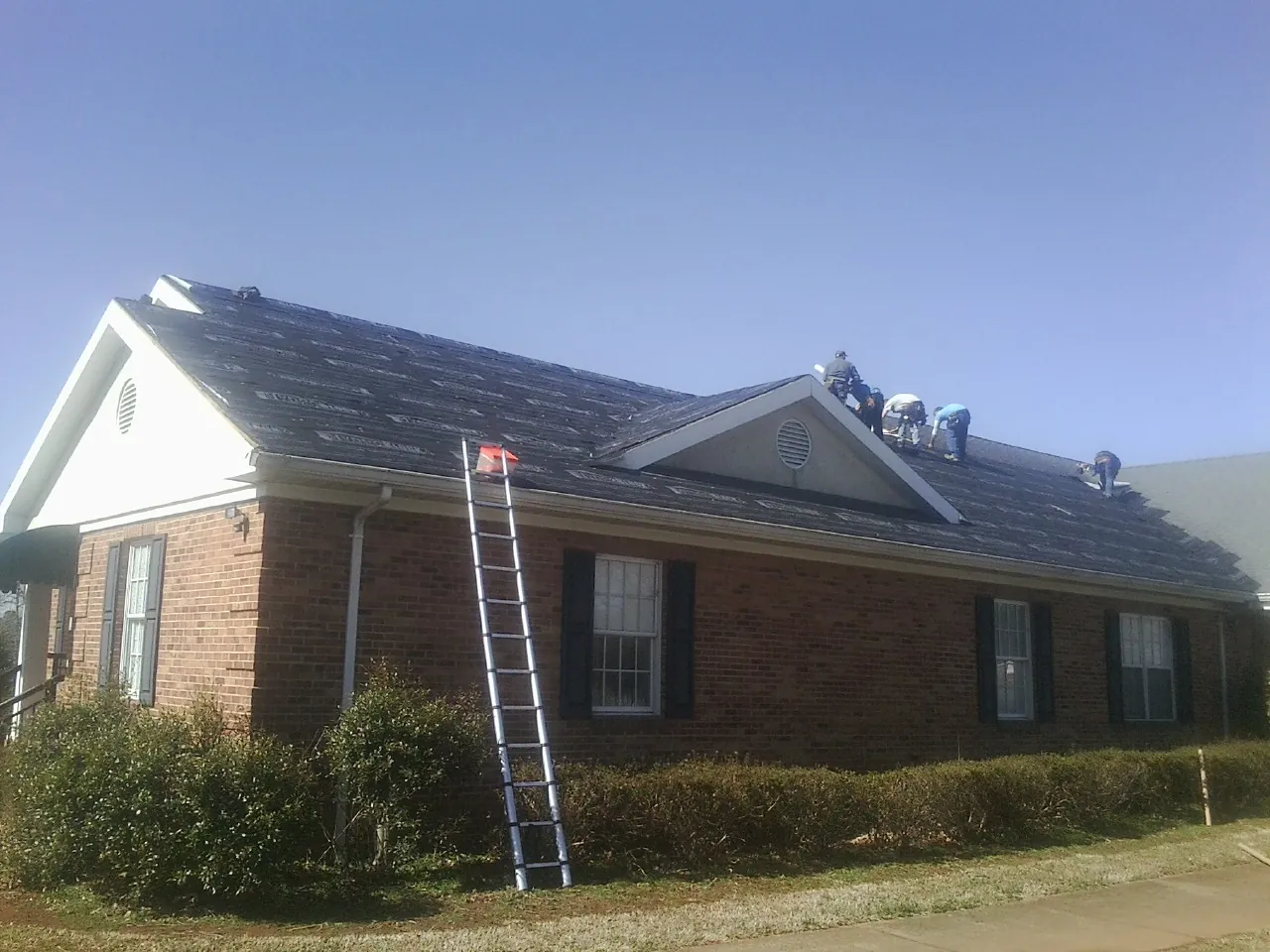 Crew tearing shingles off a brick ranch roof with a ladder set — Emergency Roof Repair work by our crew in La Mesa
