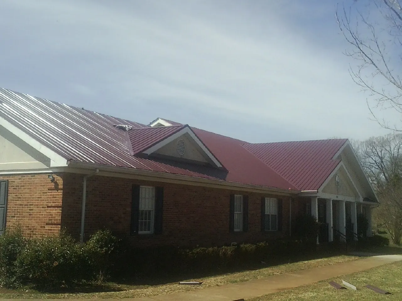 Red metal roof with gabled entries on a long brick building, from a Hail Damage Roof Repair job in La Mesa